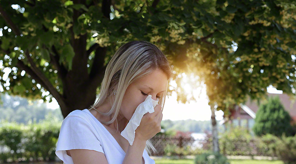 Pollen allergy. Woman sneezing in a tissue outdoors