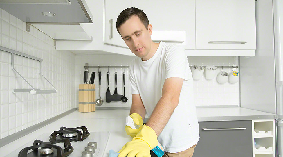 Young serious man wearing rubber yellow gloves cleaning the stov